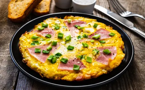 Pyszny omlet z szynką i serem, posypany szczypiorkiem, podany z grzankami. Idealny na śniadanie.