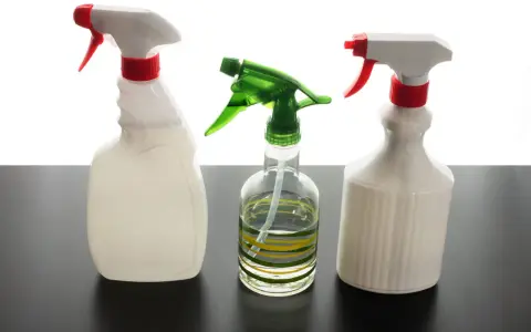 Trois flacons pulvérisateurs, dont un transparent avec des rayures vertes et jaunes, suggèrent un désinfectant naturel pour un nettoyage écologique.