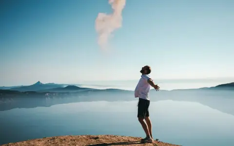 Mann mit ausgebreiteten Armen auf einem Felsvorsprung, der Rauch in den Himmel stößt. Ein Moment der Freiheit, wie Gottes Gunst.