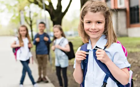 Uśmiechnięta dziewczynka z plecakiem, gotowa na zmianę szkoły średniej w 2 klasie technikum. W tle jej koledzy i koleżanki.