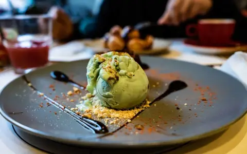 Pyszne lody pistacjowe na talerzu, ozdobione czekoladą i posypką. Idealny deser na poprawę humoru.
