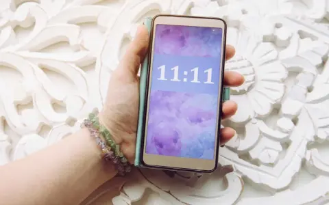 Dłoń trzyma telefon z wyświetloną godziną 11:11, co może mieć szczególne znaczenie.