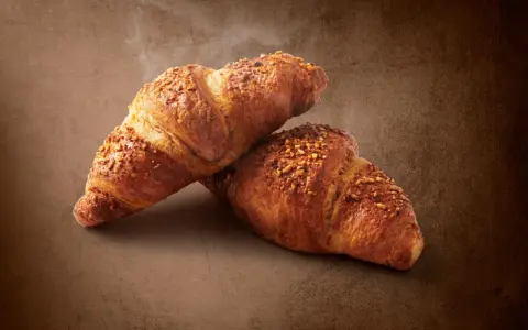 Dwa chrupiące croissanty posypane orzechami. Pyszna przekąska, ale warto pamiętać o ich kaloryczności - croissant kcal.