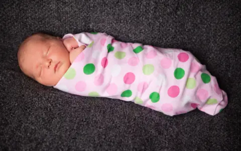 Schlafendes Baby, in rosa gepunktete Decke gewickelt. Pucken ja oder nein? Die süße Kleine scheint es zu mögen.