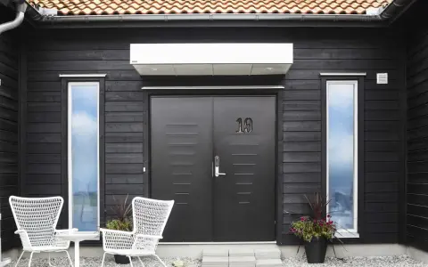 Svart trähus med dubbeldörr, nummer 19, och vita stolar. En fin inspiration framsida hus med moderna detaljer.