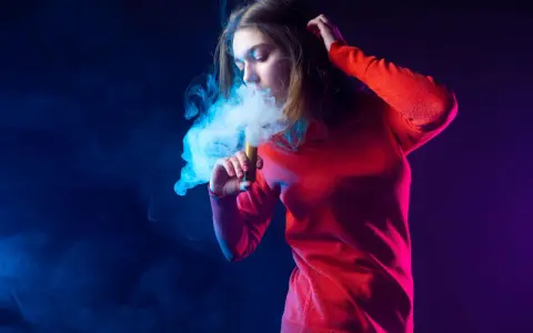 Joven exhala humo azul de un vaper. El vaper con nicotina es malo para la salud.
