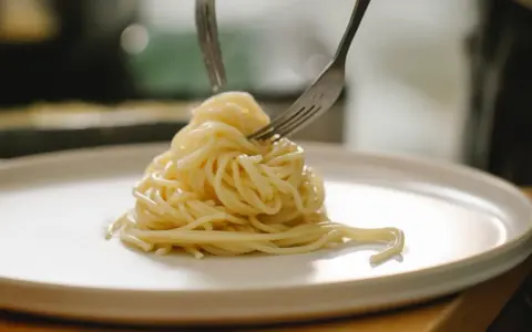 Spaghetti al limone cremosi serviti su un piatto bianco, con due forchette che li raccolgono.