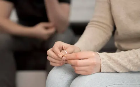 Dłoń kobiety trzyma obrączkę, symbol końca małżeństwa. Zastanawia się, jakie prawa ma niepracująca żona w takiej sytuacji.