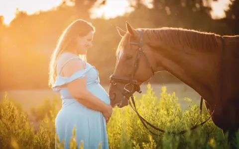 Une femme enceinte en robe bleue caresse un cheval brun au coucher du soleil. L'équitation enceinte est une belle façon de célébrer la maternité.