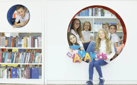 Dzieci z radością pozują z literami "AMAKids" w bibliotece.