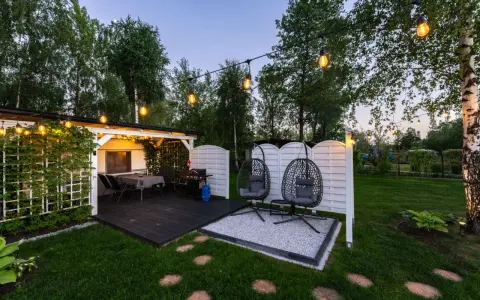 Idealne miejsce na camping w Ochabach: zadaszony taras z grillem, stolikiem i wiszącymi fotelami. Wieczorem rozświetla go girlanda żarówek.