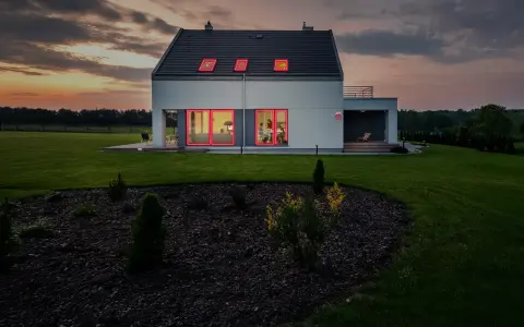 Modern villa brand med lysande röda fönsterramar mot en dramatisk solnedgång.