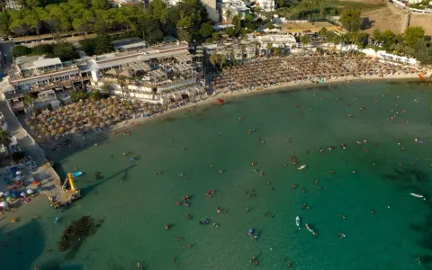 Vista aerea di una spiaggia affollata con ombrelloni e persone che nuotano nel mare cristallino, una delle spiagge più belle del mare di Taranto.
