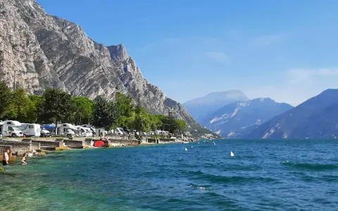 Malowniczy camping nad jeziorem Garda, z kamperami przy brzegu i górami w tle.