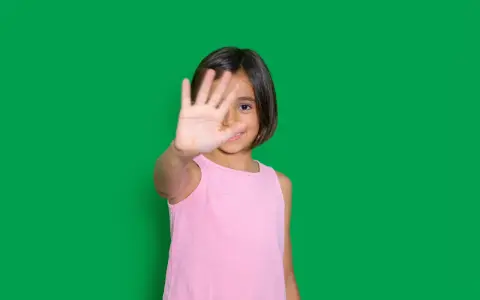 Niña de 4-5 años muestra timidez en niños, cubriendo su rostro con la mano.