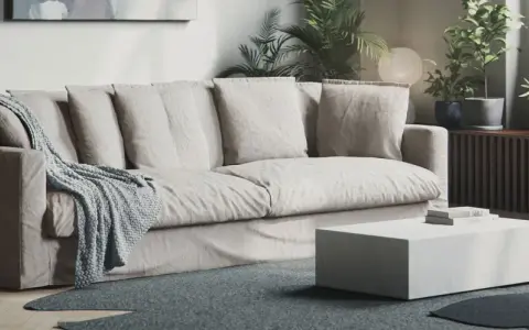 En bekväm soffa med nedsuttna dynor, prydd med en stickad pläd. Framför står ett lågt, vitt soffbord.