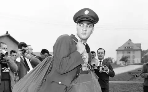 Elvis Presley 1958, in Uniform, wird von Paparazzi umringt, die mit ihren Kameras auf ihn richten.