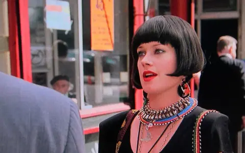 Melanie Griffith in un film, con un taglio di capelli a caschetto e un look audace.