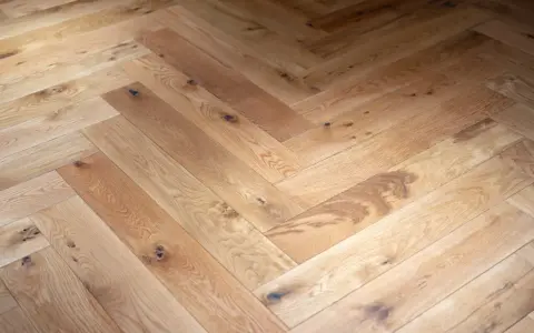 Tarima de madera en espiga, con nudos y vetas naturales, creando un patrón clásico y cálido.