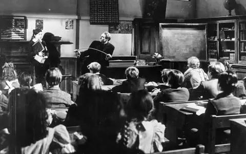 Lehrer mit Stock ermahnt Schüler in einer Klasse, die an eine Schule im Mittelalter erinnert.
