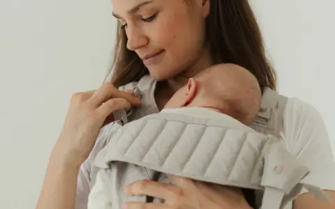 Mutter hält ihr Neugeborenes in einer Trage. Die warme Kleidung neugeborene winter schützt das Baby vor Kälte.
