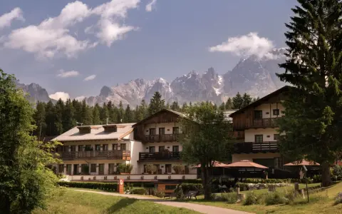 Un hotel alpino immerso nel verde, con imponenti vette innevate sullo sfondo, un perfetto scenario da montagna d'estate.