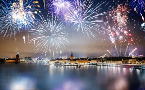 Fyrverkerier lyser upp himlen över Stockholm vid nyår. Vatten reflekterar ljusen från staden och fyrverkerierna.