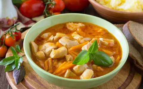 Aksamitny gulasz z piersią z kurczaka z marchewką, udekorowany bazylią. Obok kromki chleba i miska purée ziemniaczanego.