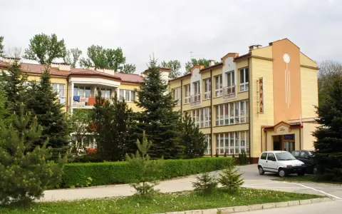 Sanatorium Rafał Busko Zdrój, z żółtą fasadą i zielenią wokół, zaprasza na wypoczynek.