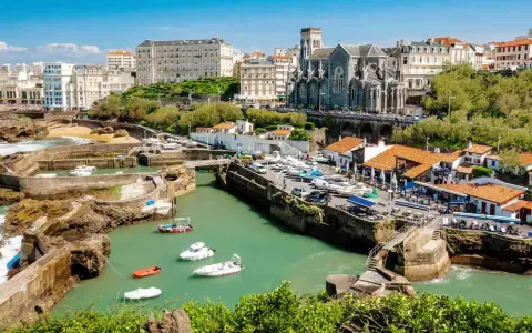 En vacker vy över hamnen i Biarritz med båtar i vattnet och en kyrka i bakgrunden. Kanske är det här tåg till Biarritz tar dig.
