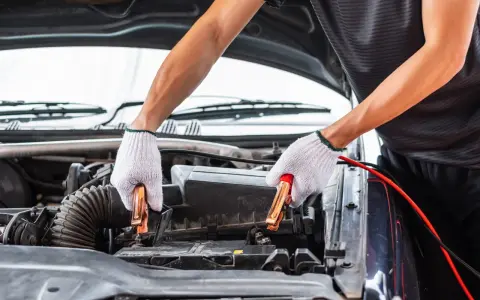 Hands in white gloves connect jumper cables to a car battery. This process helps answer how long does it take to charge a car battery.