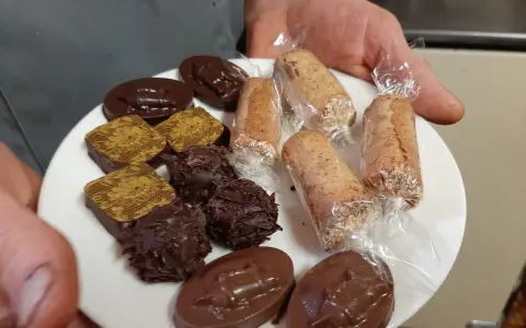 Assortiment de chocolats et biscuits, dont une spécialité d'Alençon, présentés sur une assiette blanche.