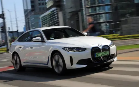 Białe BMW i4 w ruchu miejskim, z widocznymi światłami LED i grillem.