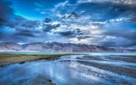 Paesaggio montano con lago e fiume, cielo drammatico con nuvole scure e luna, effetto HDR.