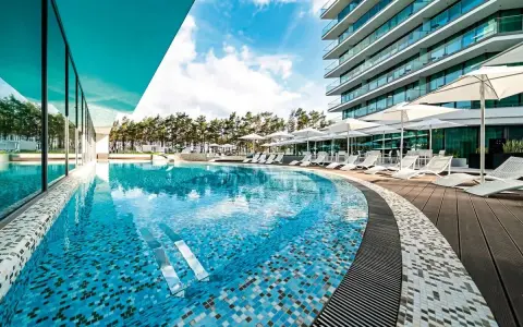 Luksusowy basen z mozaiką i leżakami, otoczony sosnami, przy nowoczesnym hotelu. Idealne miejsce na relaks, jak na plaży w Międzyzdrojach.