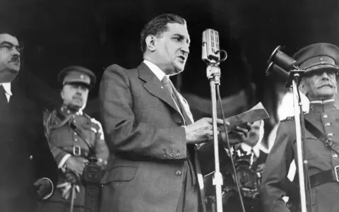 Un homme en costume parle à un microphone, entouré d'officiers en uniforme. Un moment clé de la dictature portugaise de Salazar.