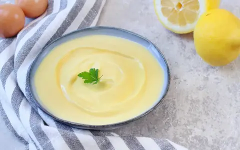 Cremige Joghurt-Mayonnaise mit Zitrone und Petersilie, daneben Eier und Zitronen.