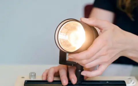 Händer justerar en lampa, kanske för att ta bort dimmer. Ljuset är starkt.