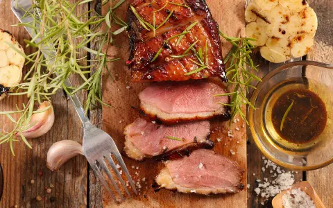 Magret de canard tranché, servi avec une sauce pour magret de canard, romarin, ail rôti et gros sel.