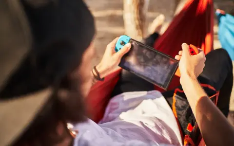 Osoba w hamaku gra na Nintendo Switch. Czas ładowania konsoli jest krótki, więc można grać wszędzie.
