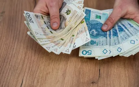 Dłonie trzymające stosy polskich banknotów 200 zł i 50 zł, być może na sześciomiesięczną odprawę emerytalną.