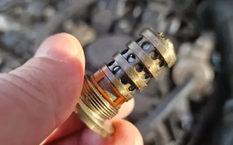 Dłoń trzyma zabrudzony zawór zmiennych faz rozrządu, gotowy do czyszczenia.