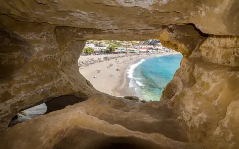 Blick durch Höhle auf Strand von Matala, Kreta. Ein sonniges Hippie-Dorf mit bunten Häusern und blauem Meer.
