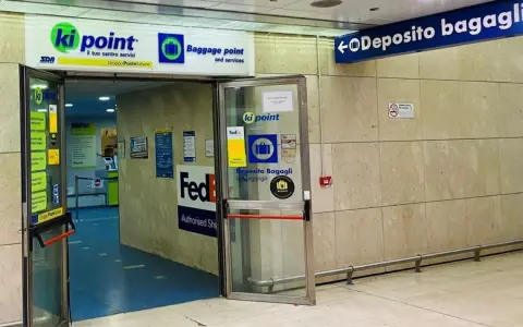 Entrance to a Ki Point baggage storage facility with signage for "Deposito Bagagli" and FedEx.