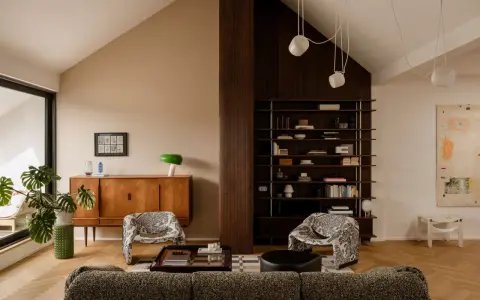 Salón acogedor con **techo inclinado interior**, muebles de madera, estanterías y sillones estampados.