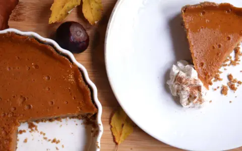 La tarta de calabaza de la abuela, con su relleno cremoso y corteza dorada, lista para ser disfrutada. Una rebanada servida con nata montada y canela.