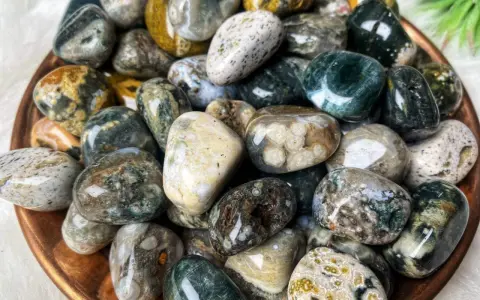 Montón de piedras jaspe blanco pulidas, con vetas verdes, marrones y amarillas. Sus propiedades son conocidas por su conexión con la naturaleza.