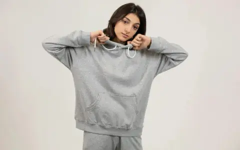 Dziewczyna w szarej bluzie oversize, z kapturem naciągniętym na głowę, pokazuje, jak nosić ten wygodny element garderoby.