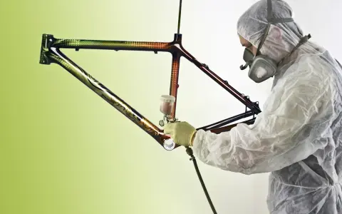 Person in Schutzanzug lackiert kunstvoll einen Rennrad Rahmen mit Spraydose.