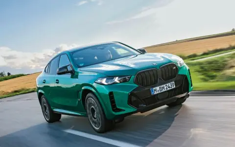 Zielony suv coupe pędzi po drodze, otoczony polami i błękitnym niebem.